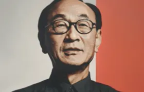 Older man in round black glasses against a split grey and orange background