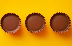 Three unwrapped milk chocolate peanut butter cups on a bright yellow background