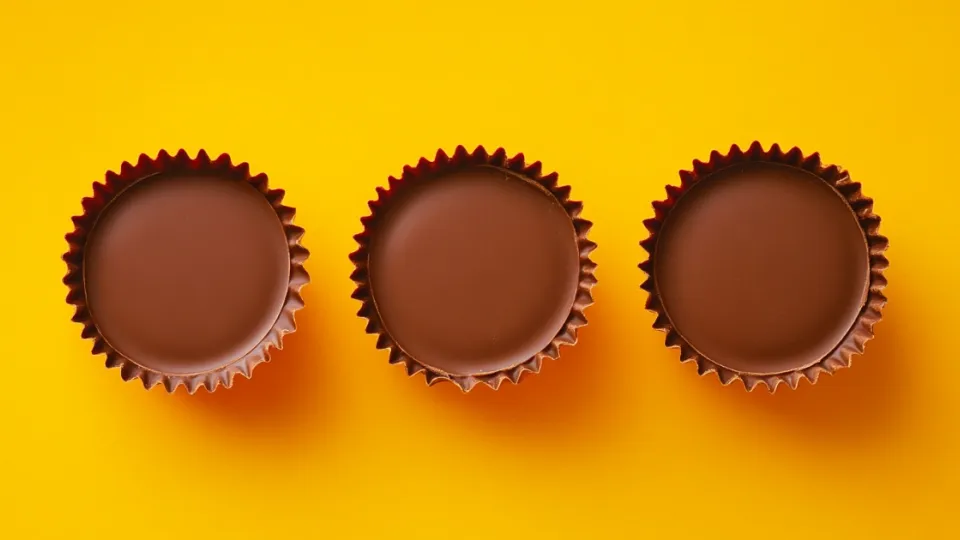 Three unwrapped milk chocolate peanut butter cups on a bright yellow background