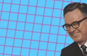 Herman Lay smiling in horn-rimmed glasses and suit on pink grid
