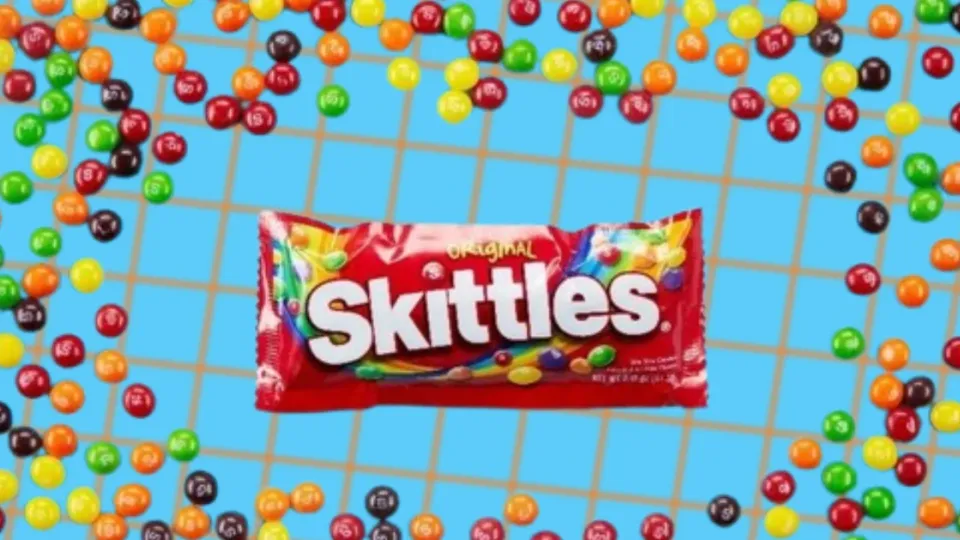 Original Skittles bag surrounded by scattered rainbow Skittles candies