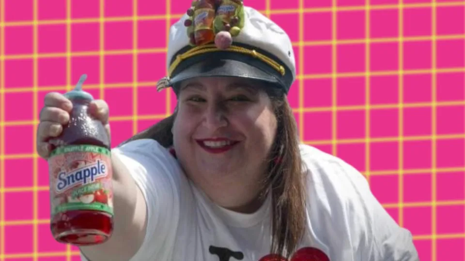 Wendy Kaufman holding a Snapple Apple bottle in a fruit-topped captain hat