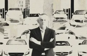 Man in dark suit with arms crossed before rows of parked rental cars