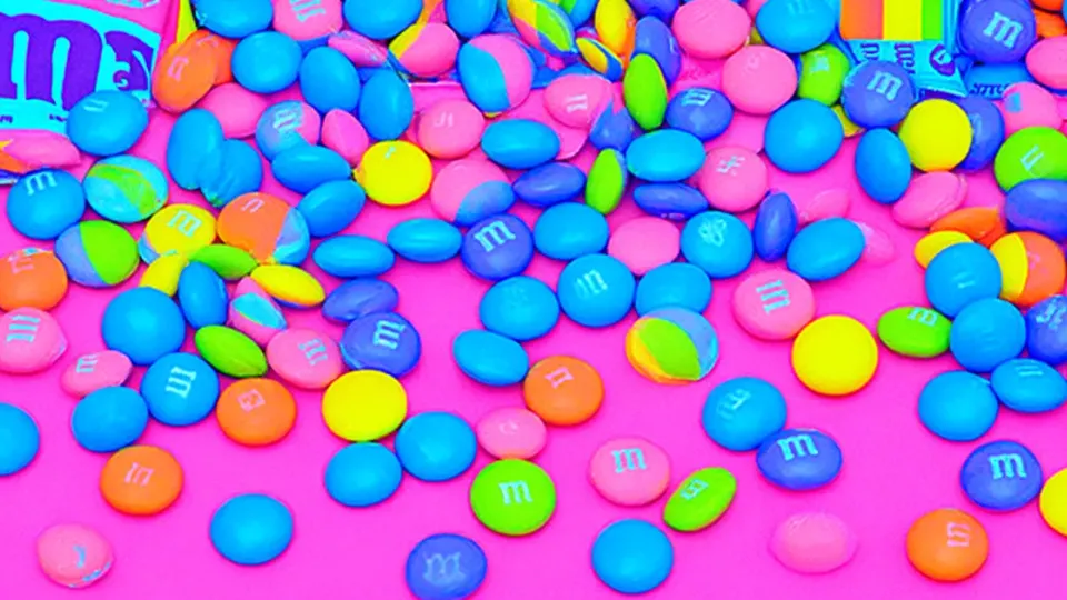 Colorful M&M’s candies scattered on bright pink background