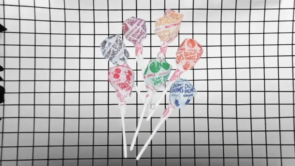 Seven wrapped Dum-Dums lollipops against a black and white grid