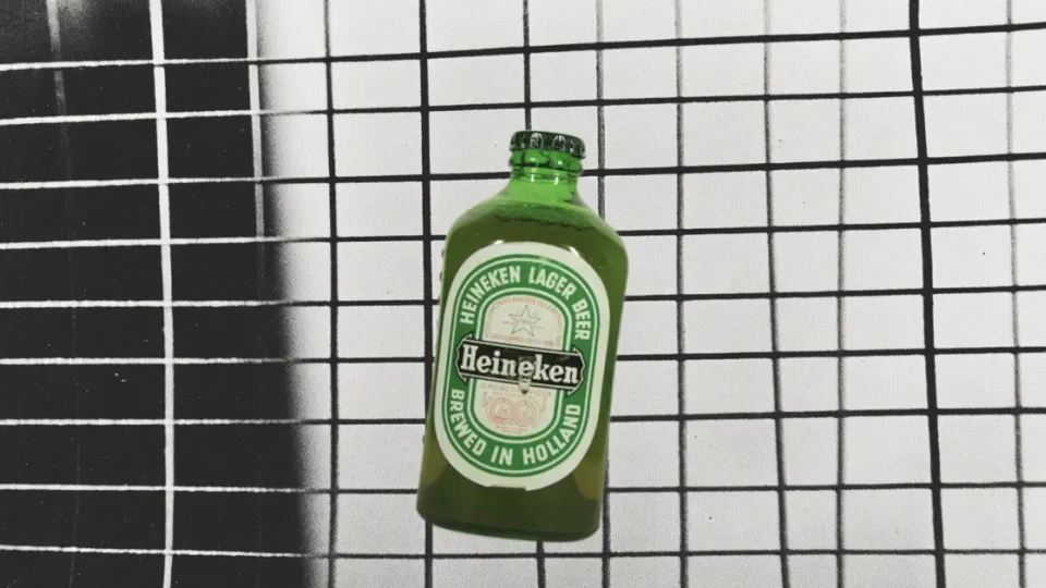 Green Heineken lager beer bottle against a black-and-white tiled wall