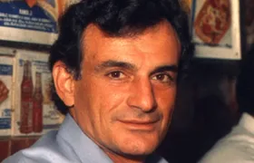 Fred DeLuca smiling in a light blue shirt inside an early sandwich shop